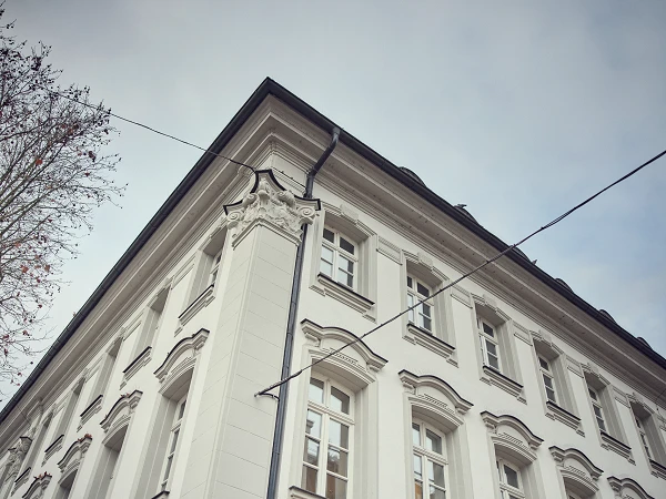 Ein weiße, historische Gebäudeecke mit aufwendigen Verzierungen und Fenstern, unter einem bewölkten Himmel.