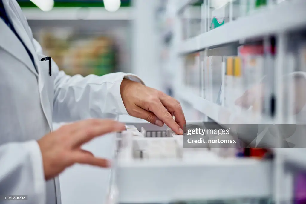 Ein Apotheker in weißem Kittel ordnet Medikamente in einer offenen Schublade in einer Apotheke.