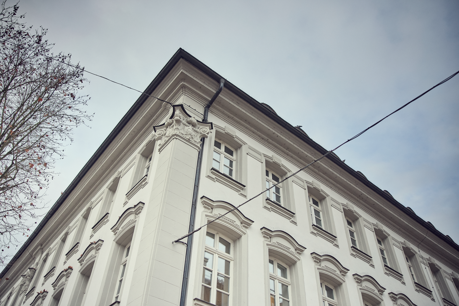 Ein weiße, historische Gebäudeecke mit aufwendigen Verzierungen und Fenstern, unter einem bewölkten Himmel.